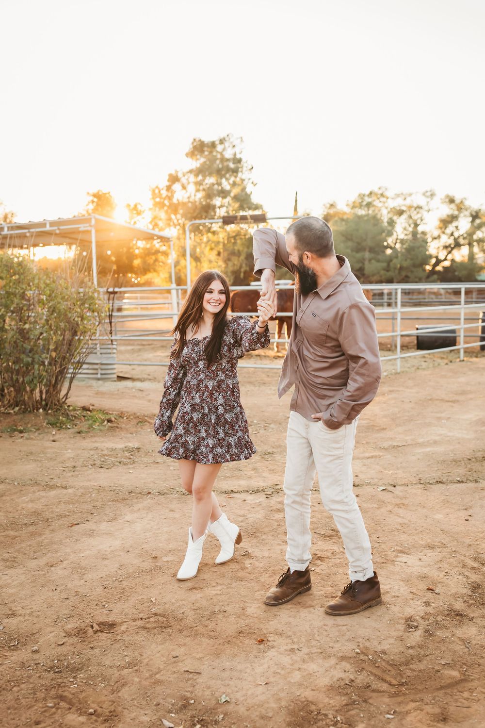 A couple dancing together at golden hour on a ranch with horse paddocks in the background.