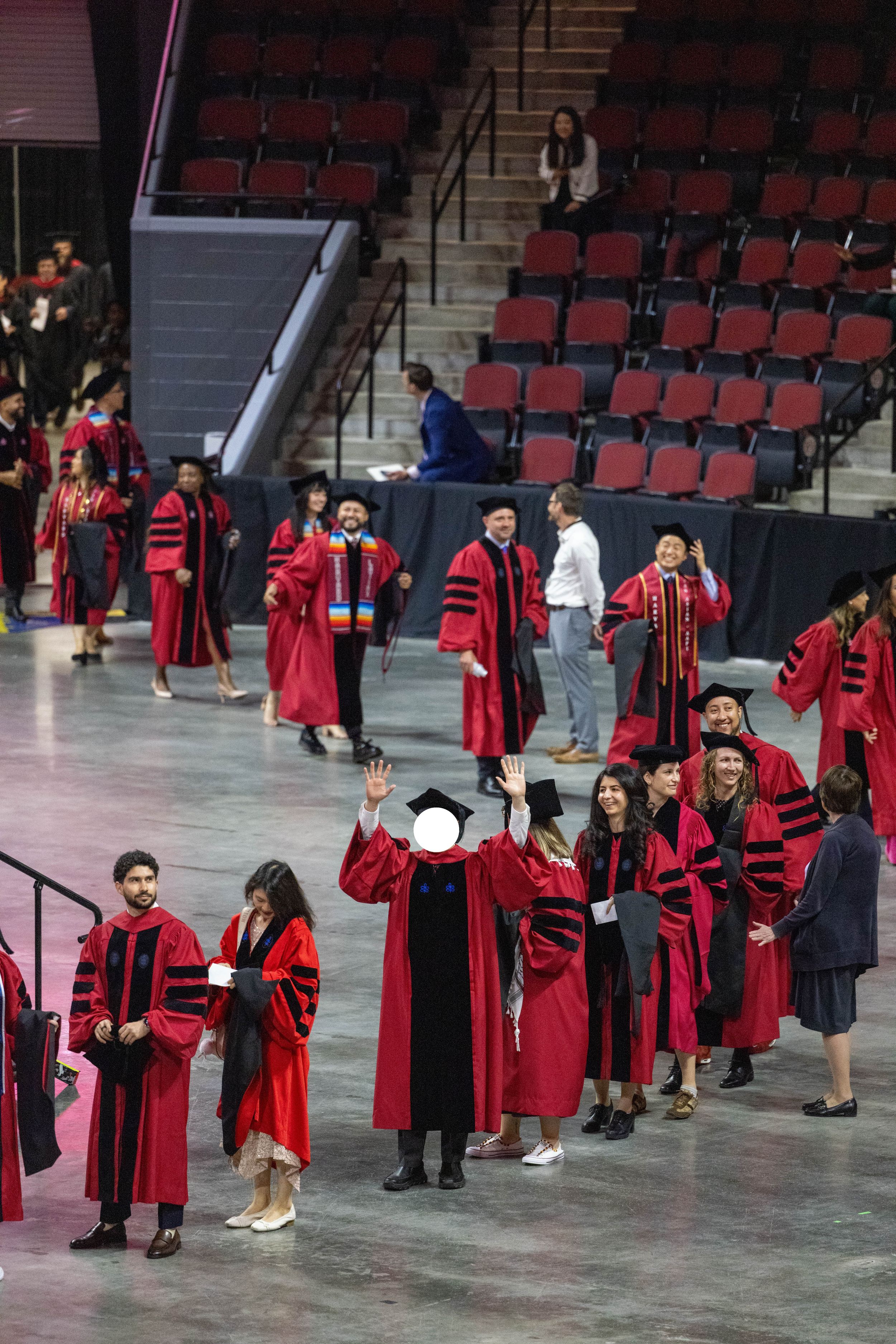Graduates in red doctoral robes process through an arena during a university commencement ceremony.