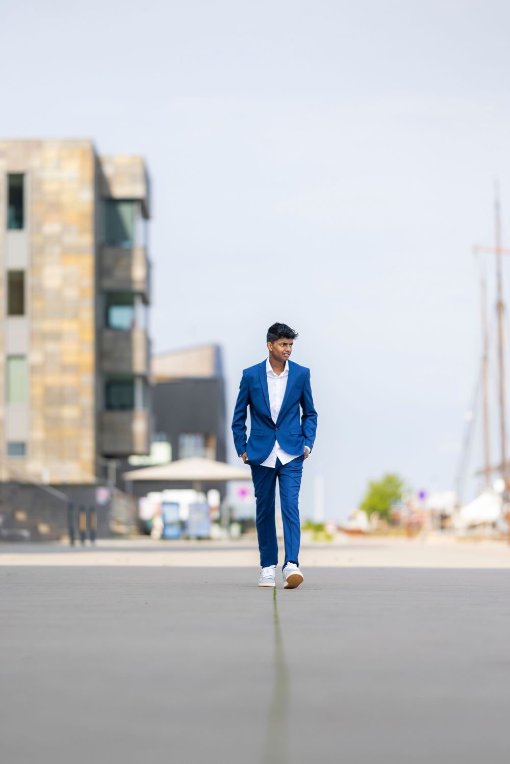 Young man in a blue suit walking confidently outdoors near a modern building on a clear day.