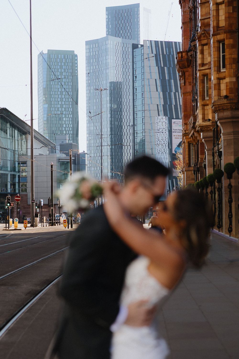 Bride and groom share a romantic embrace on a city street with modern skyscrapers in the background.