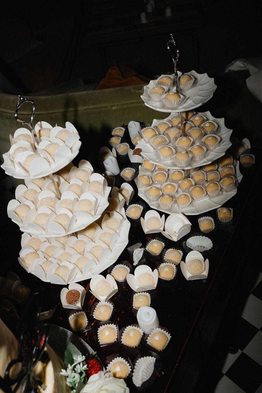 Elegant tiered dessert stands filled with white paper-wrapped sweets and golden truffles at a wedding reception in Manchester.