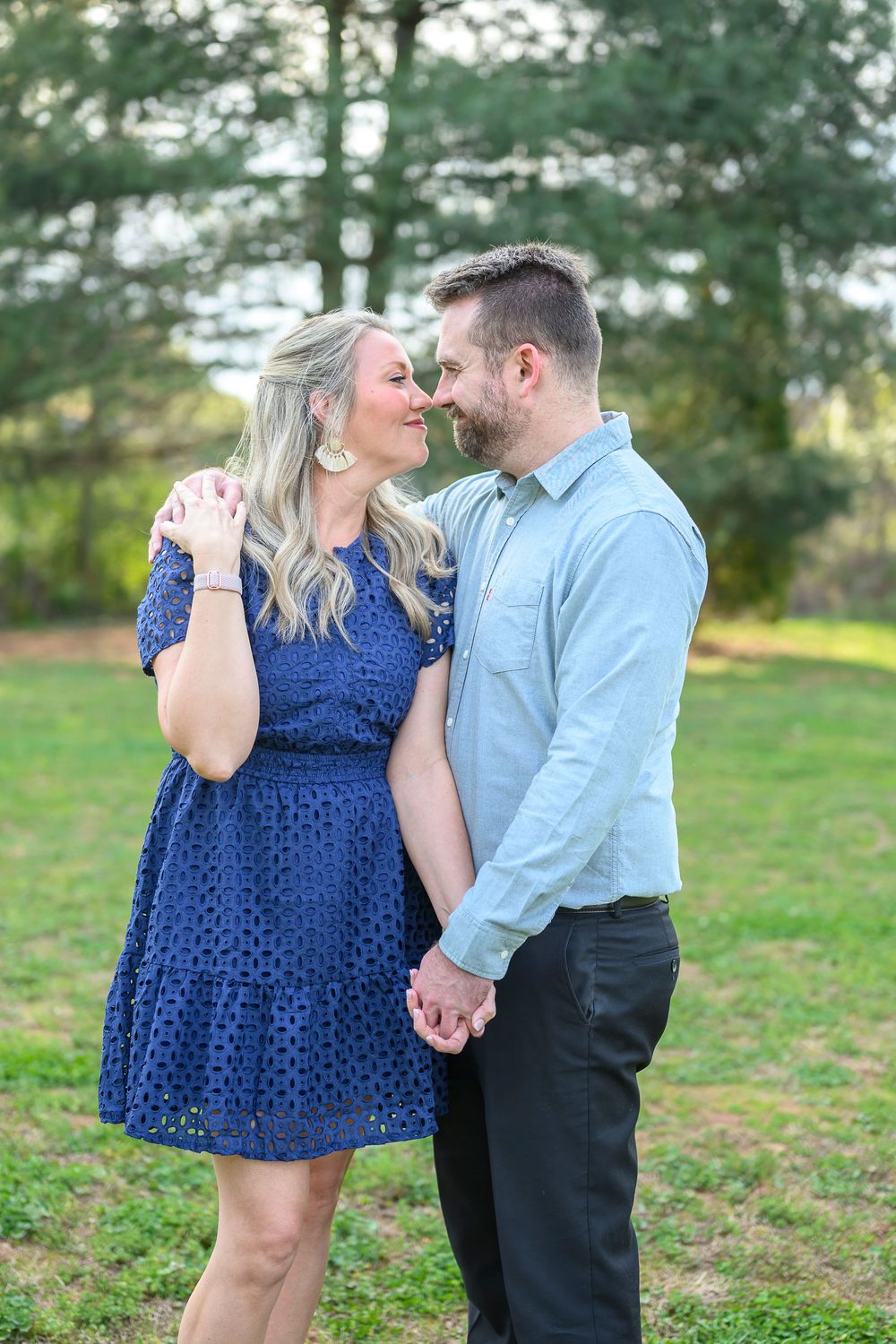 A couple shares a romantic moment outdoors, the woman in a blue lace dress holding hands with a man in a light blue shirt.
