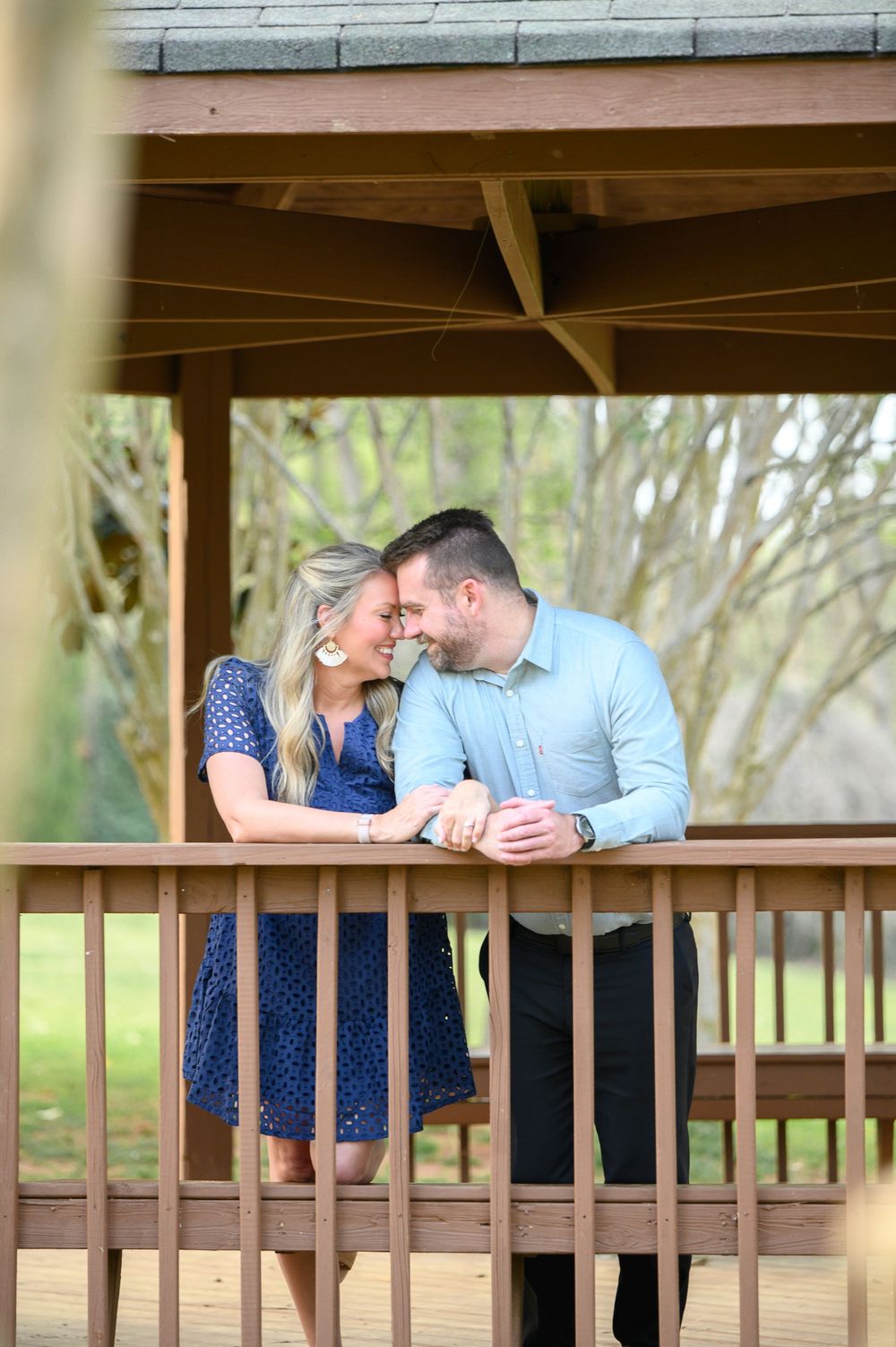 Couple sharing a romantic moment on a wooden gazebo deck, woman in navy dress and man in light blue shirt.