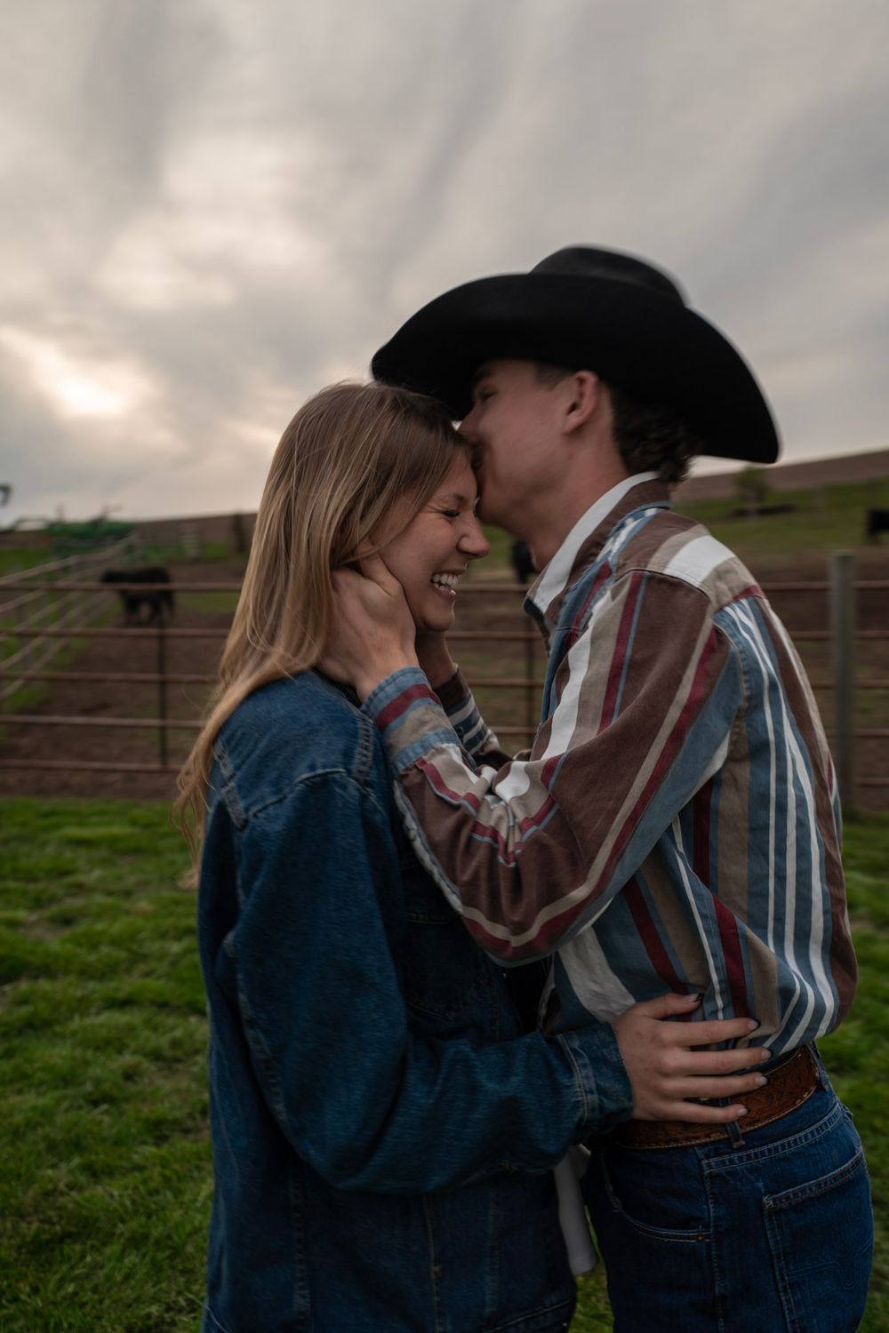 A couple shares a romantic moment on a farm, with the man in a cowboy hat and plaid shirt gently holding the woman's face.