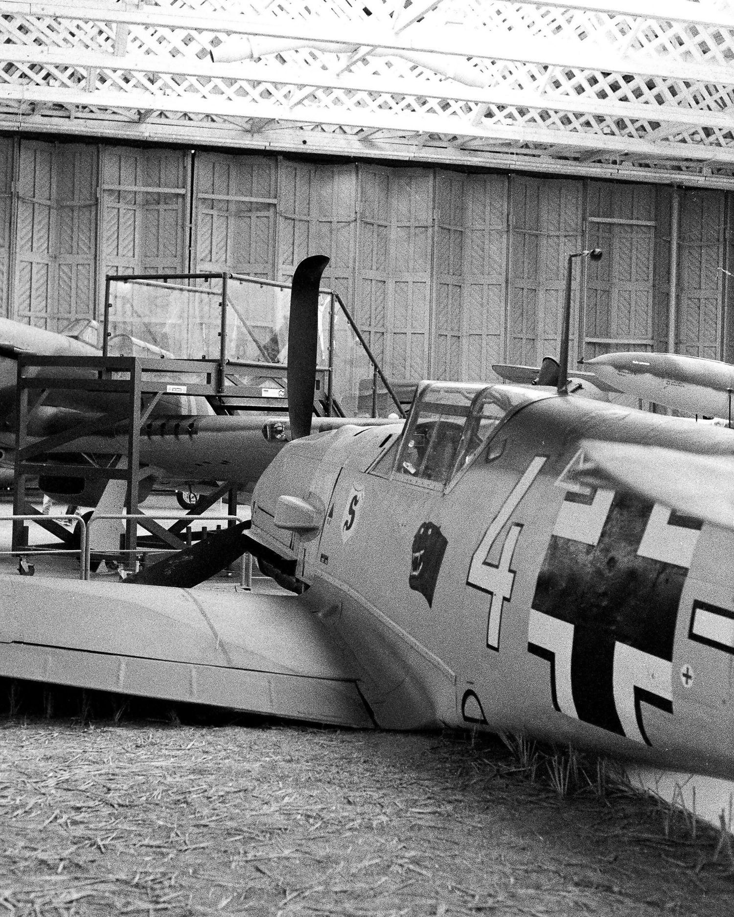 Black and white photo of a WWII German Messerschmitt Bf 109 fighter aircraft with Luftwaffe markings parked near a hangar.