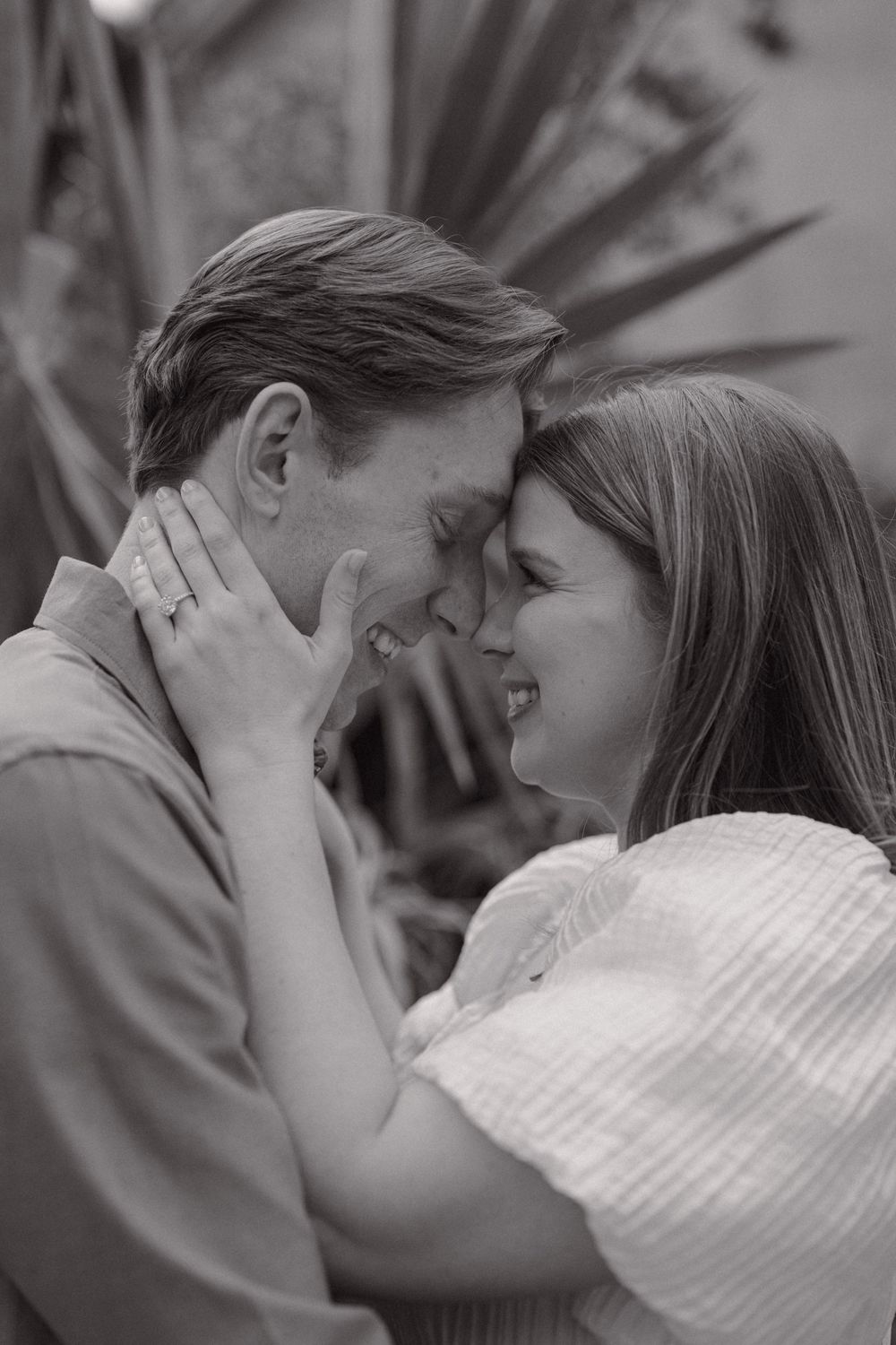 Black and white photo of a happy couple smiling and touching foreheads outdoors.