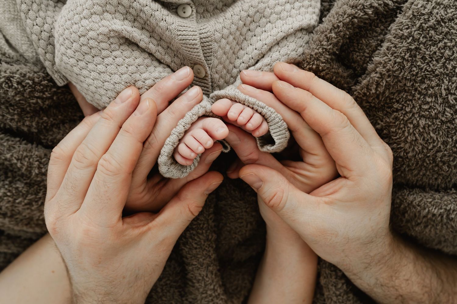 Detailfoto von Babyfüßchen gehalten von Mama's und Papa's Händen beim Newbornfotoshooting Wien