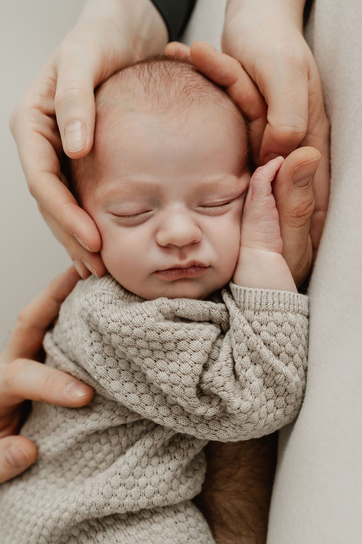 geborgenes Foto eines schlafenden Neugeborenen in den Händen der Eltern beim Babyfotoshooting Stockerau