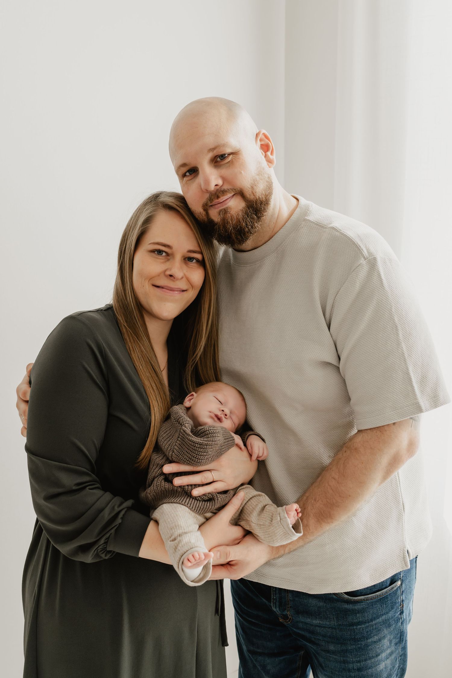 Eltern mit ihrem schlafenden Neugeborenen im Arm beim Babyfotoshooting Wien