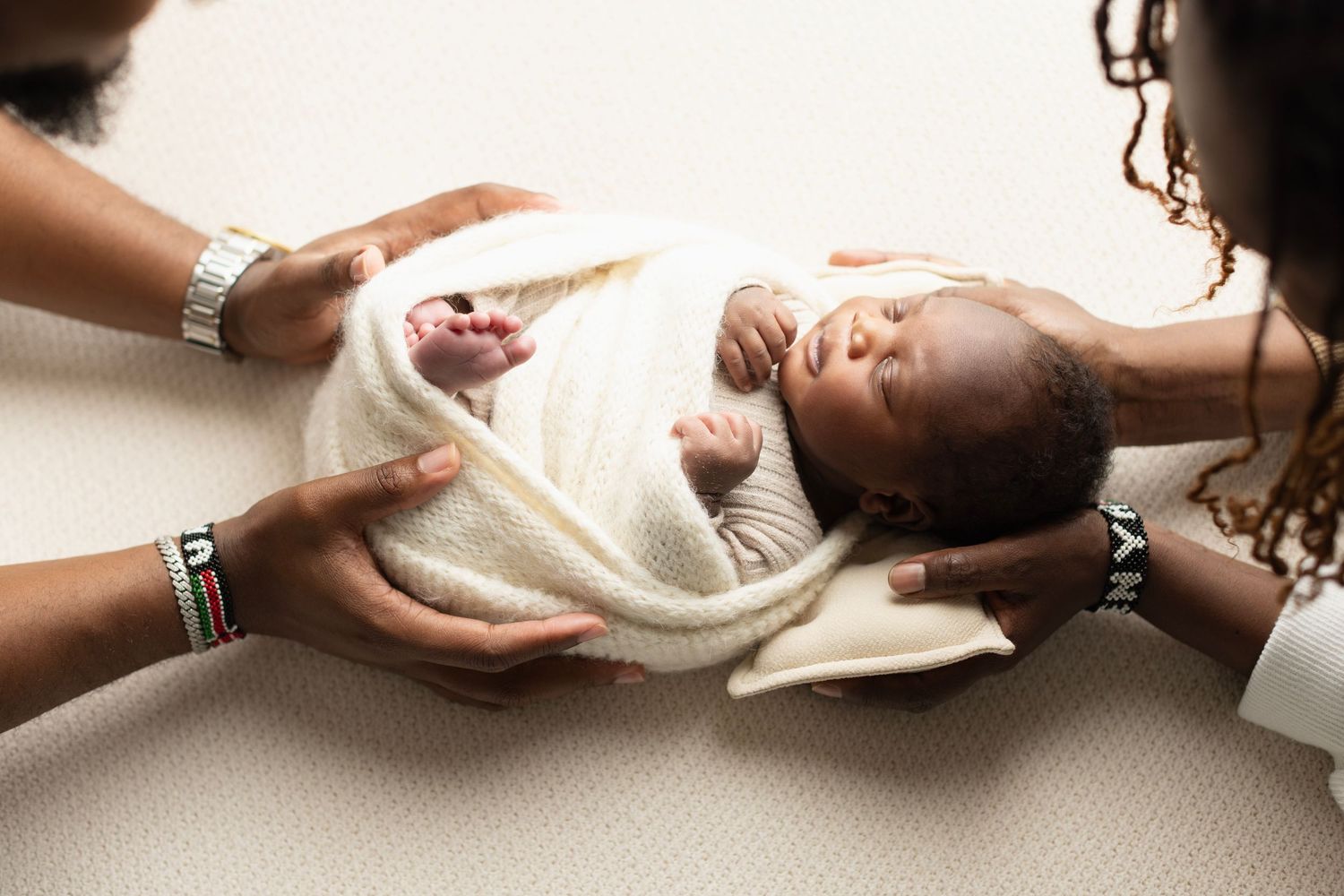 Two adults gently holding a swaddled newborn baby wrapped in a white blanket during a newborn photography session. Elizabeth Lang Photograph