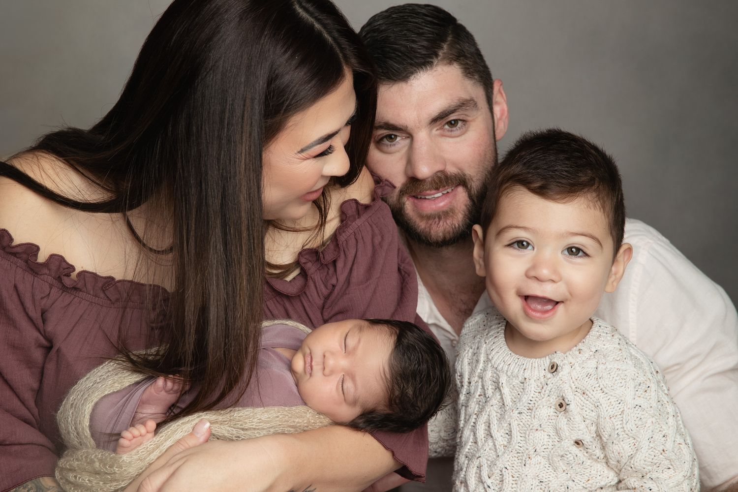 Happy family of four with newborn baby and toddler posing together in professional studio portrait.