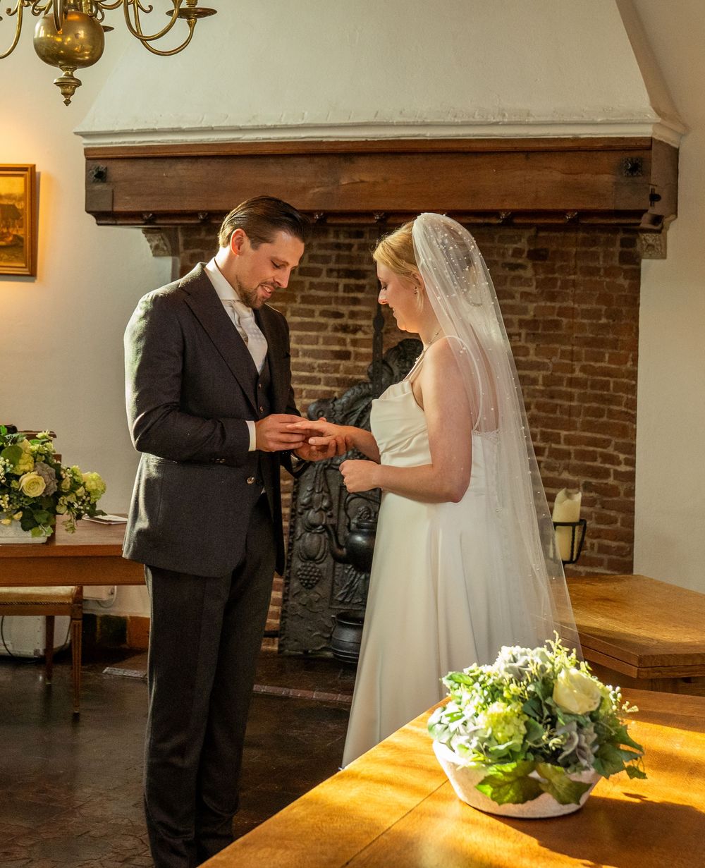 De bruidegom schuift de trouwring om de vinger van de bruid tijdens een intieme ceremonie naast een rustieke bakstenen open haard