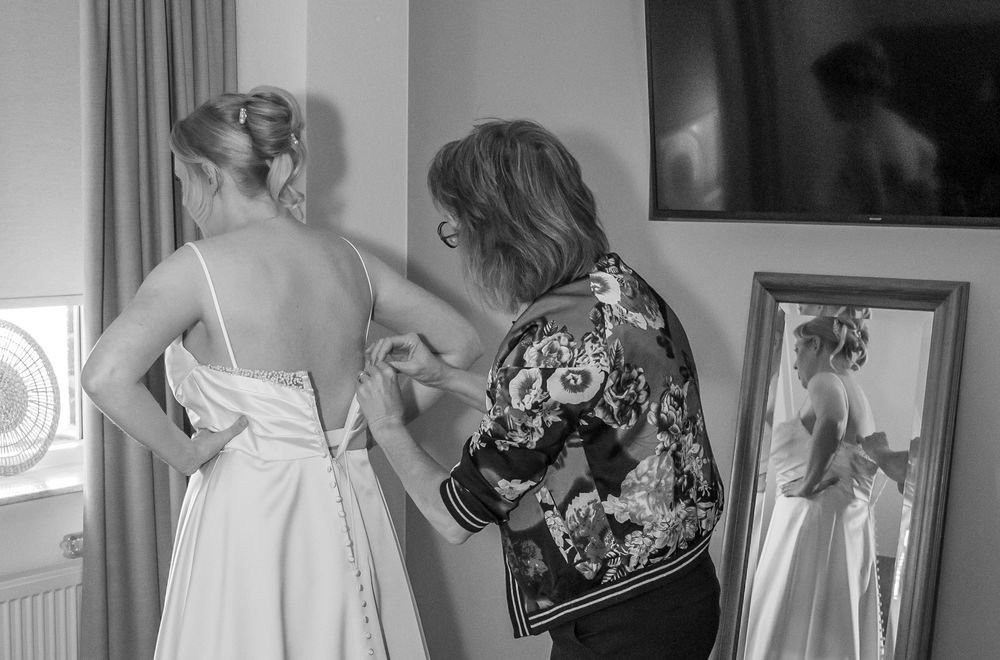 Zwart-witfoto van een vrouw die de bruid helpt haar trouwjurk dicht te maken voor de ceremonie.