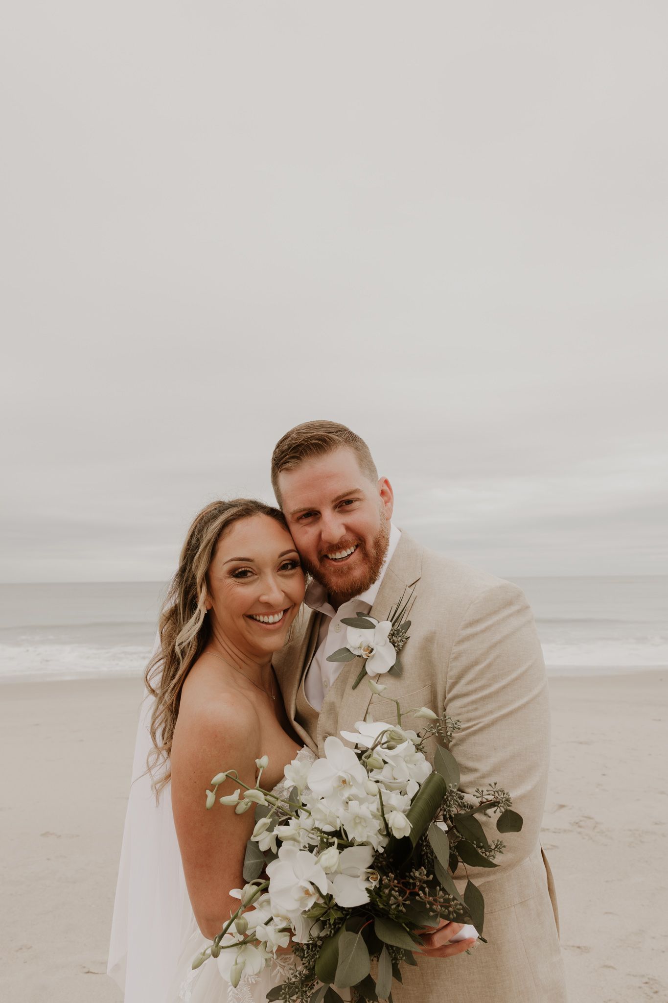 A bride and groom share a romantic kiss in a lush outdoor setting, with the bride holding a vibrant pink and red bouquet.