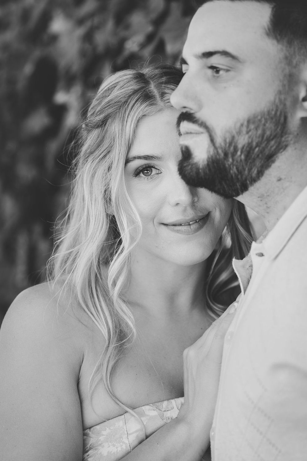 Black and white romantic couple portrait with bearded man kissing womans cheek outdoors.