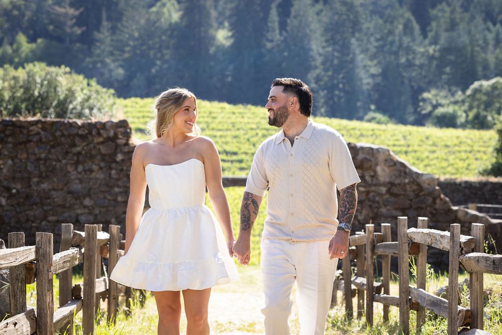 Happy couple holding hands walking through a scenic vineyard on their wedding day.