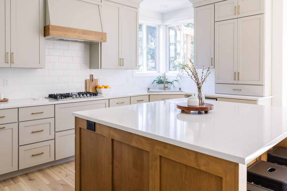 A modern kitchen featuring white quartz countertops, wood island accents, and gray shaker cabinets.