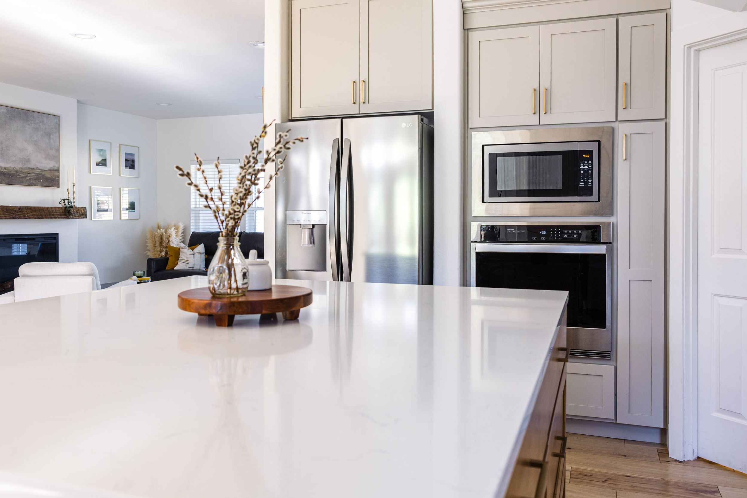 Bright kitchen featuring a large white quartz island, gray cabinets, stainless steel refrigerator, and built-in microwave.