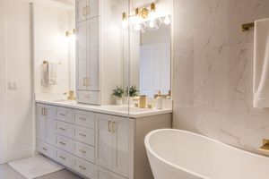 Spa-like master bathroom featuring dual vanity with gold fixtures, freestanding tub, and floor-to-ceiling marble tile.