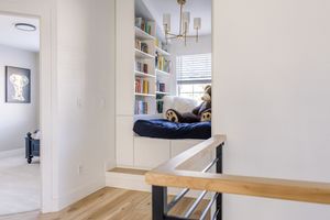 Cozy reading nook with built-in white bookshelves, navy window seat cushion, and modern staircase railing.