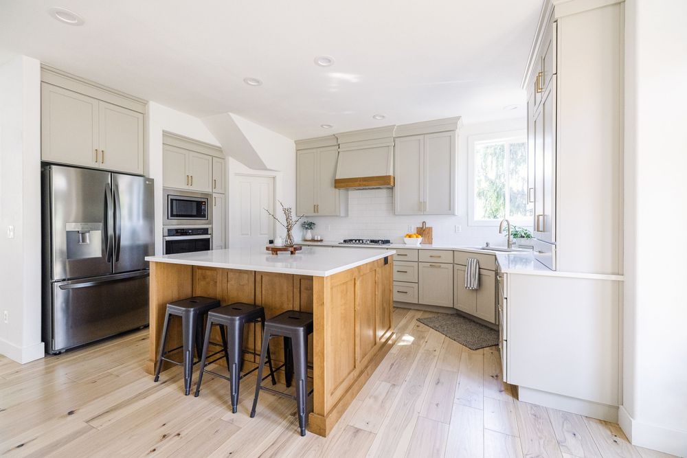 Contemporary kitchen featuring gray cabinets, wood-paneled island with bar stools, stainless appliances, and white countertops.