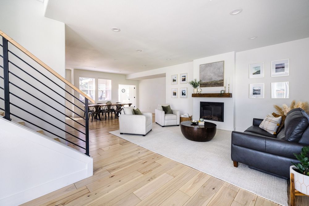 Modern open-concept living room with light hardwood floors, black stair railing, stone fireplace, and neutral decor.