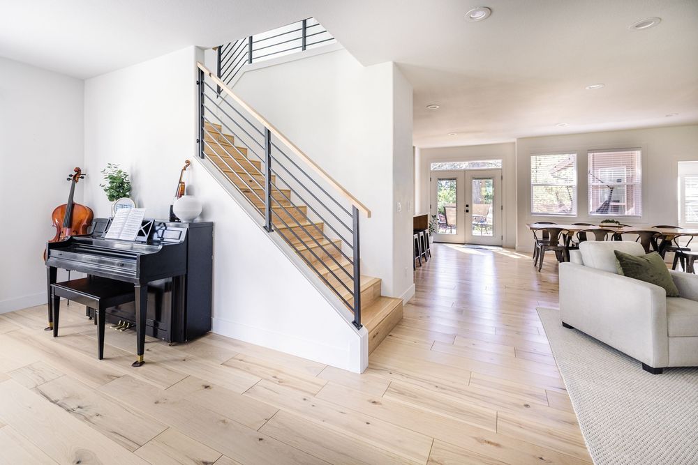Modern home entryway with light hardwood floors, open staircase with metal railings, and a grand piano near the stairs.