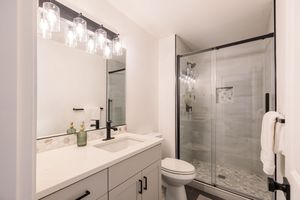 Contemporary bathroom with glass shower, white vanity, marble countertop, and pendant lighting fixtures.