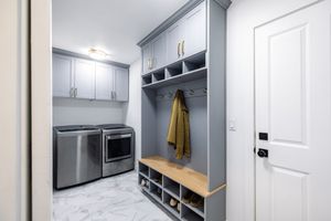 Gray mudroom with built-in cubbies, bench seating, shoe storage, and stainless steel washer and dryer.
