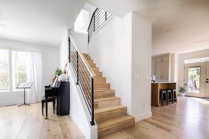 Bright modern staircase with wood steps, black metal railings, skylight above, and light hardwood floors.