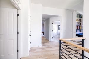 Open upstairs hallway with light hardwood floors, white walls, black door hardware, and built-in bookshelves.