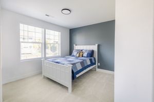 Simple bedroom with white bed frame, blue accent wall, neutral carpet, and double windows.