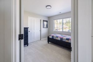 Small bedroom with dark bed frame, closet door, neutral carpet, and single window with natural light.