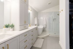 Elegant master bathroom with gray cabinets, gold hardware, freestanding tub, and walk-in shower.