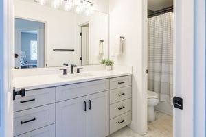 Modern white bathroom vanity with gray cabinets, black fixtures, large mirror, and shower.