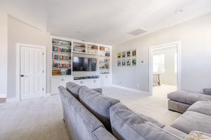 Cozy living room with built-in white shelving, large TV, gray sectional sofa, and plush carpet.