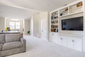 Bright living area featuring white built-in cabinets, flat-screen TV, bookshelves, and soft carpet.