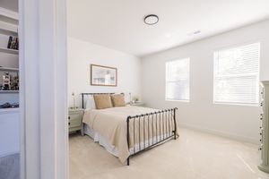 Minimalist bedroom with iron bed frame, neutral bedding, two windows, and light tile flooring.
