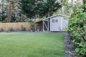 Landscaped backyard with lush green lawn, gray garden shed, wooden fence, and mature trees.