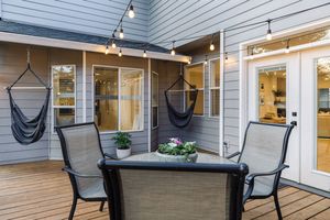 Cozy backyard deck with string lights, hanging hammock chairs, outdoor dining set, and French doors.