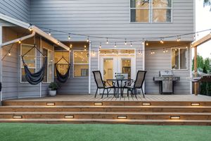 Elegant backyard deck at dusk with string lights, hammock chairs, dining set, and step lighting.