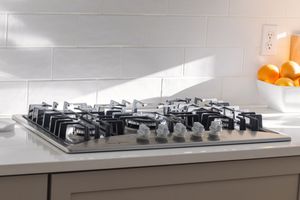 Stainless steel five-burner gas cooktop installed in white kitchen counter with subway tile backsplash.