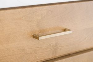 Close-up of brushed gold rectangular drawer pull on natural light wood cabinet drawer.