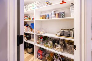 Well-organized walk-in pantry with white shelves stocked with food, containers, and small kitchen appliances.