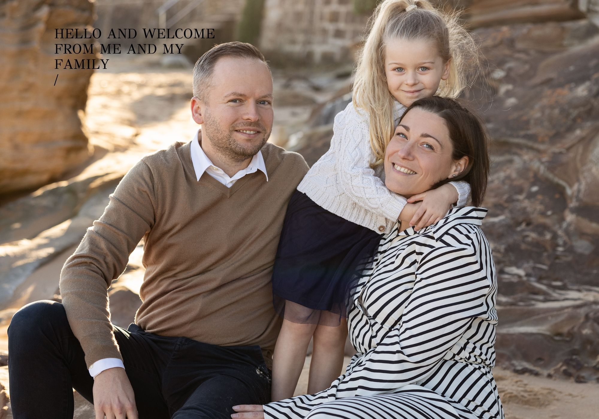 Family of three poses for casual outdoor portrait against stone wall.