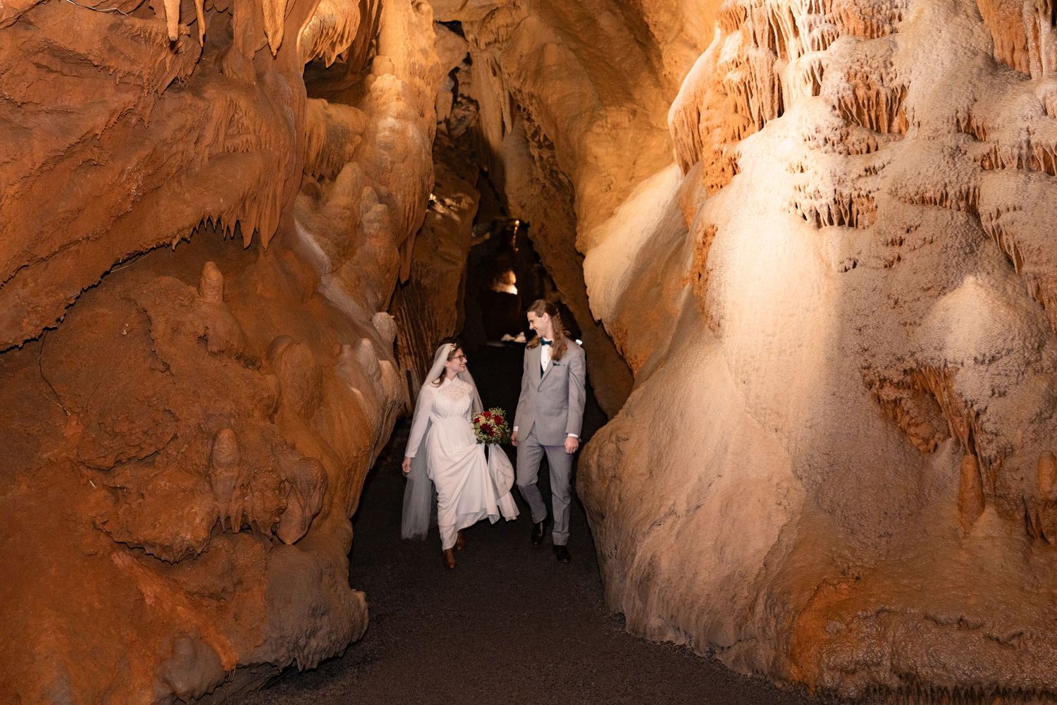 Bride and groom walking hand in hand through a stunning cave with glowing stalactites and stalagmites.