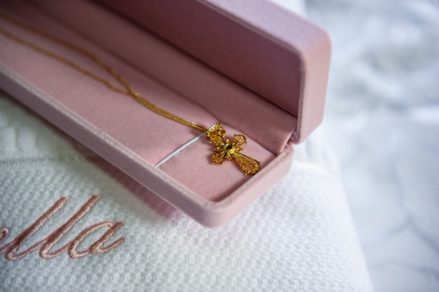 Gold cross pendant necklace in pink velvet jewelry box on white embroidered cloth.