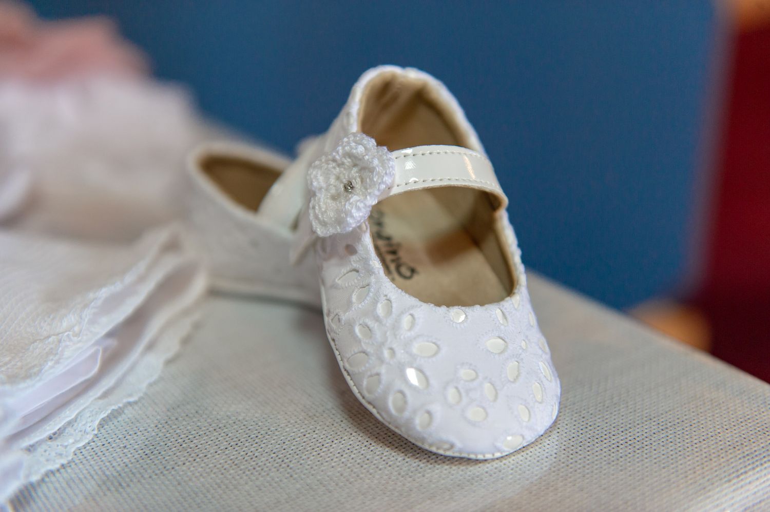 White baby girl baptism shoe with floral embroidery and bow detail on white surface.