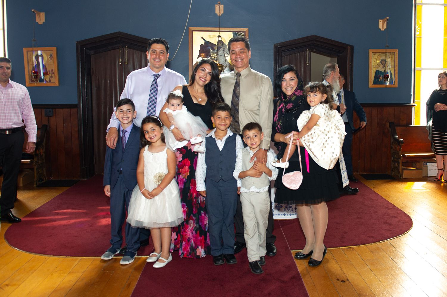 Extended family group photo at Orthodox Christian baptism ceremony inside decorated church.