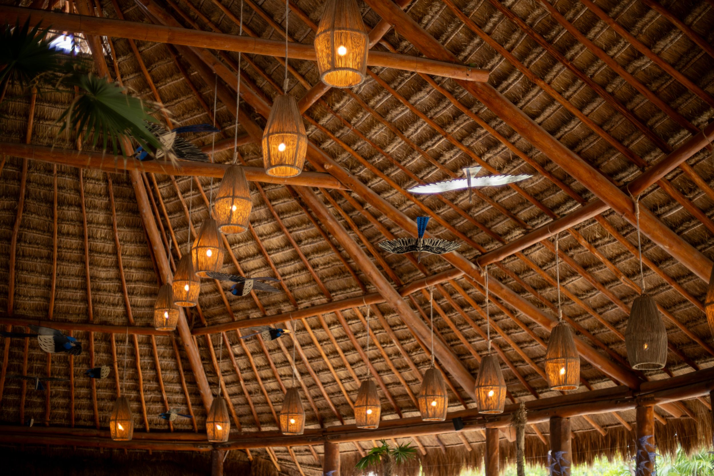 Rustic bamboo thatched roof interior with hanging wicker lanterns and ceiling fans in a tropical open-air pavilion.